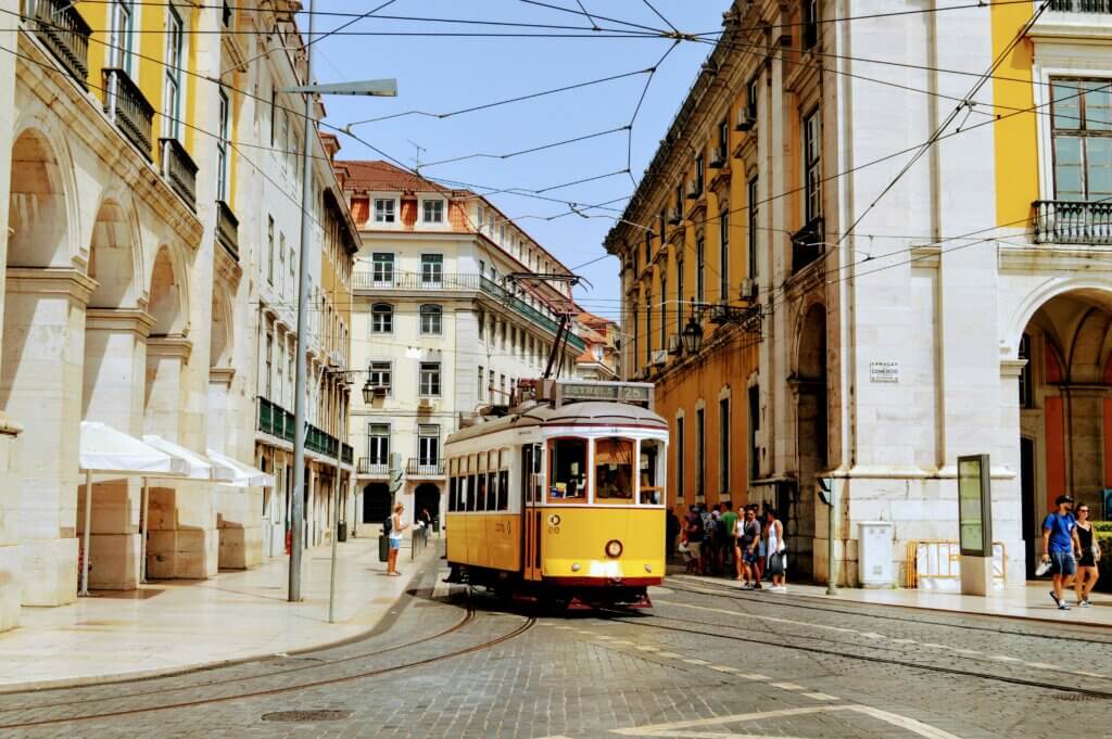 Yellow tram moving through the historic streets of Lisbon, Portugal, with classic architecture in the background.