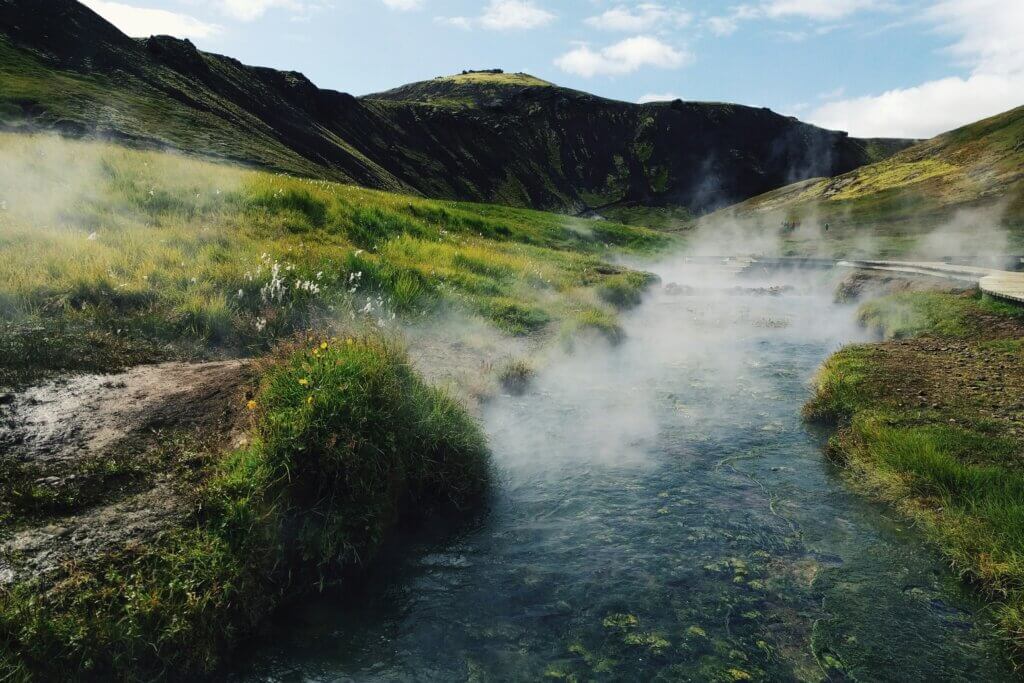 A stunning Icelandic hot spring surrounded by snow-covered mountains and steam rising from the water.