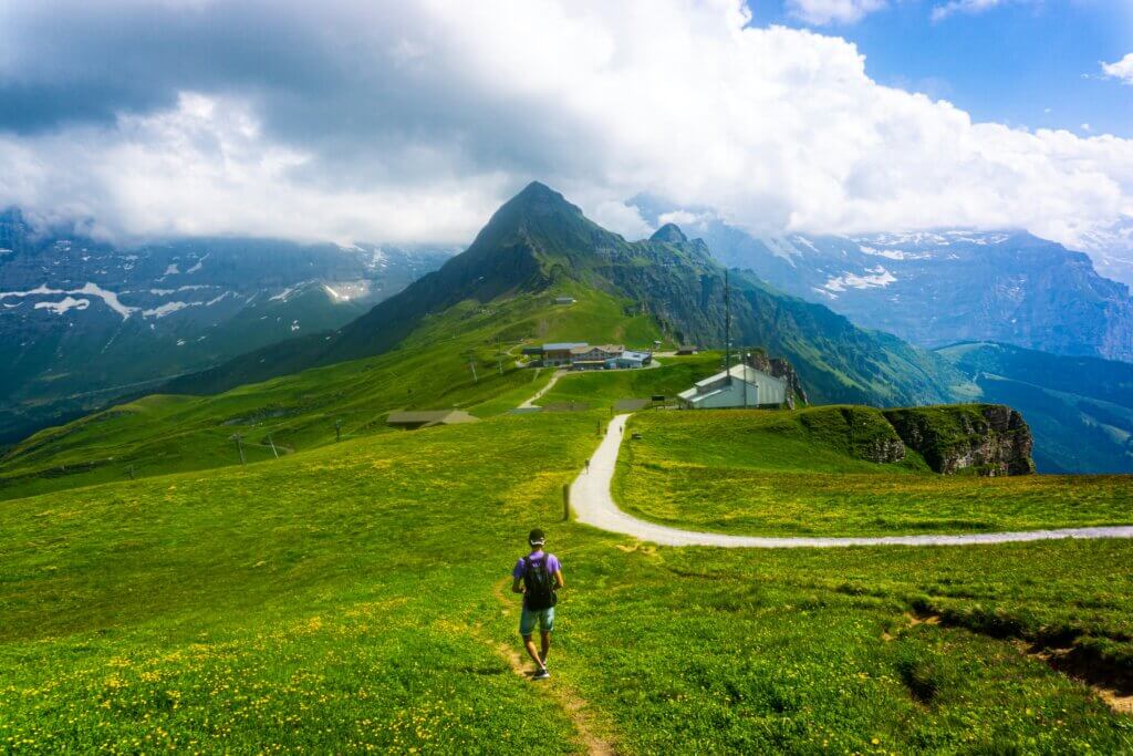 Rustic wooden chalets of Gimmelwald perched on a green alpine slope overlooking the Lauterbrunnen Valley and distant peaks